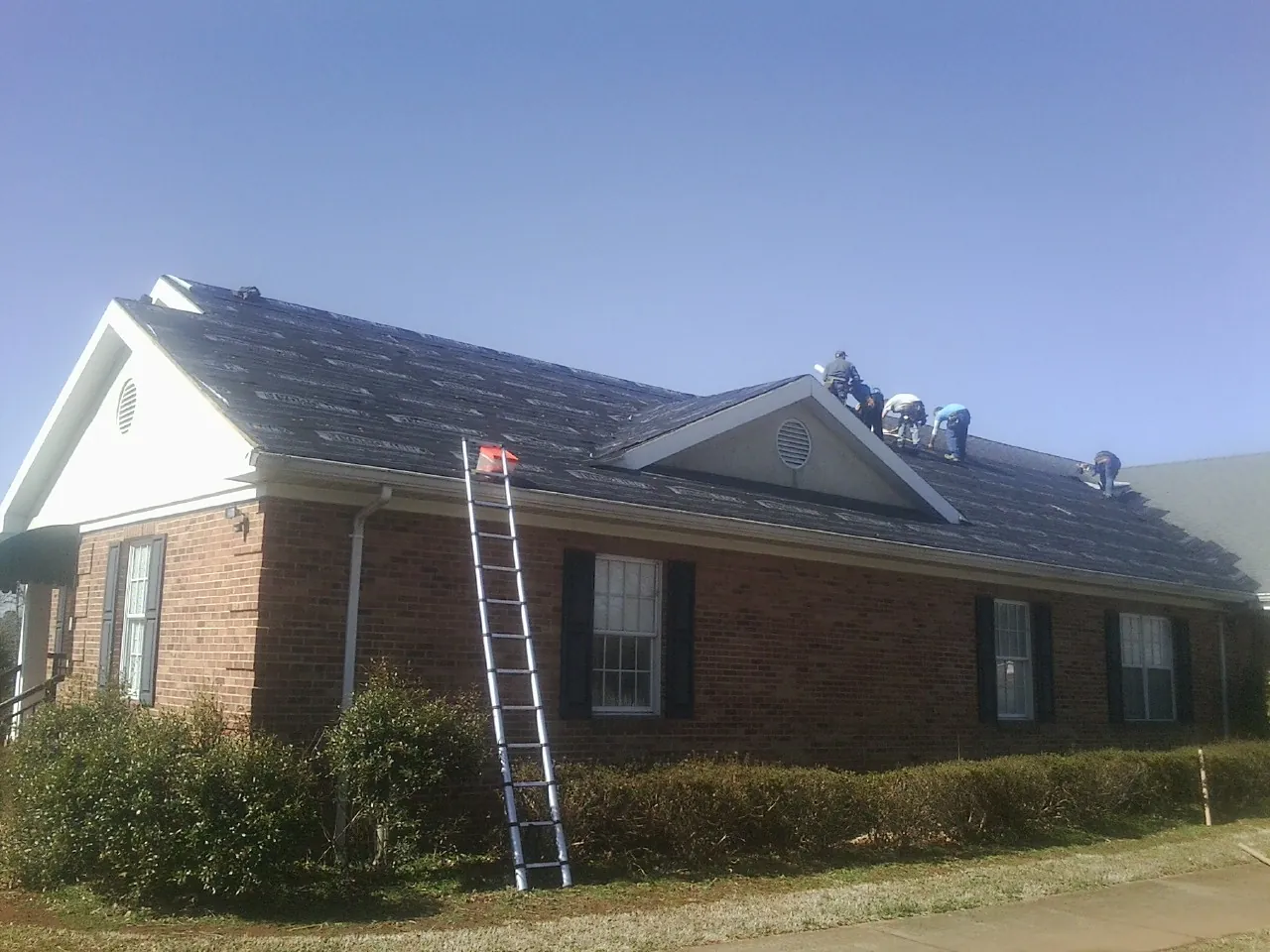 Crew tearing shingles off a brick ranch roof with a ladder set — Metal Roof Repair work by our crew in York Haven