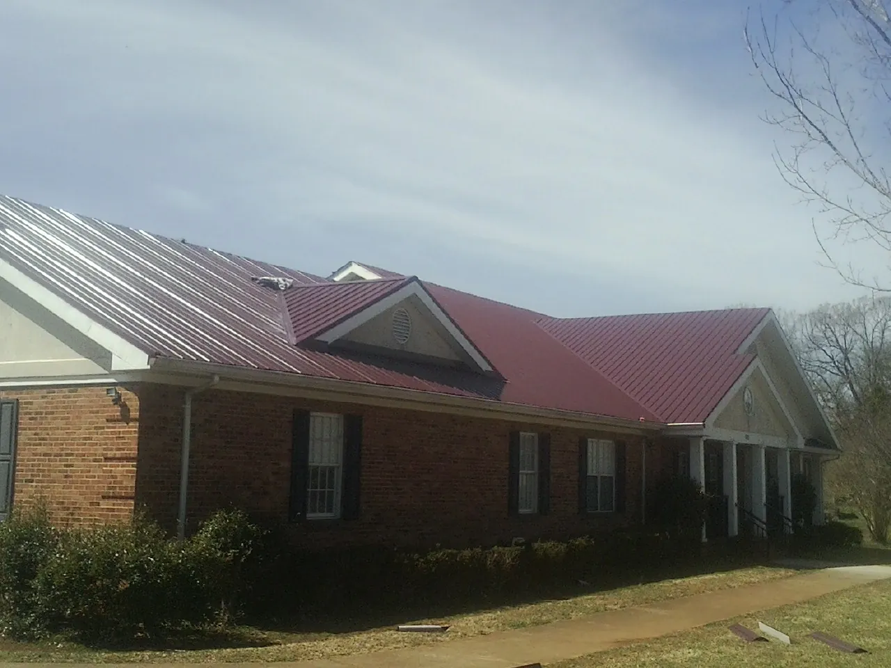 Red metal roof with gabled entries on a long brick building, from a Hail Damage Roof Repair job in York Haven