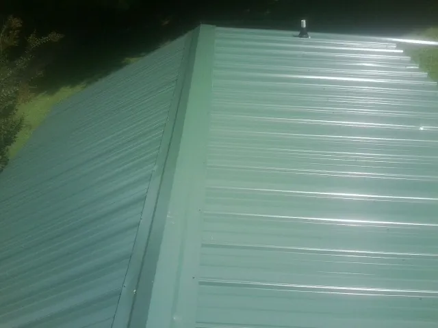 New green metal panels meeting at the ridge of a roof — Flat Roof Repair work by our crew in York Haven