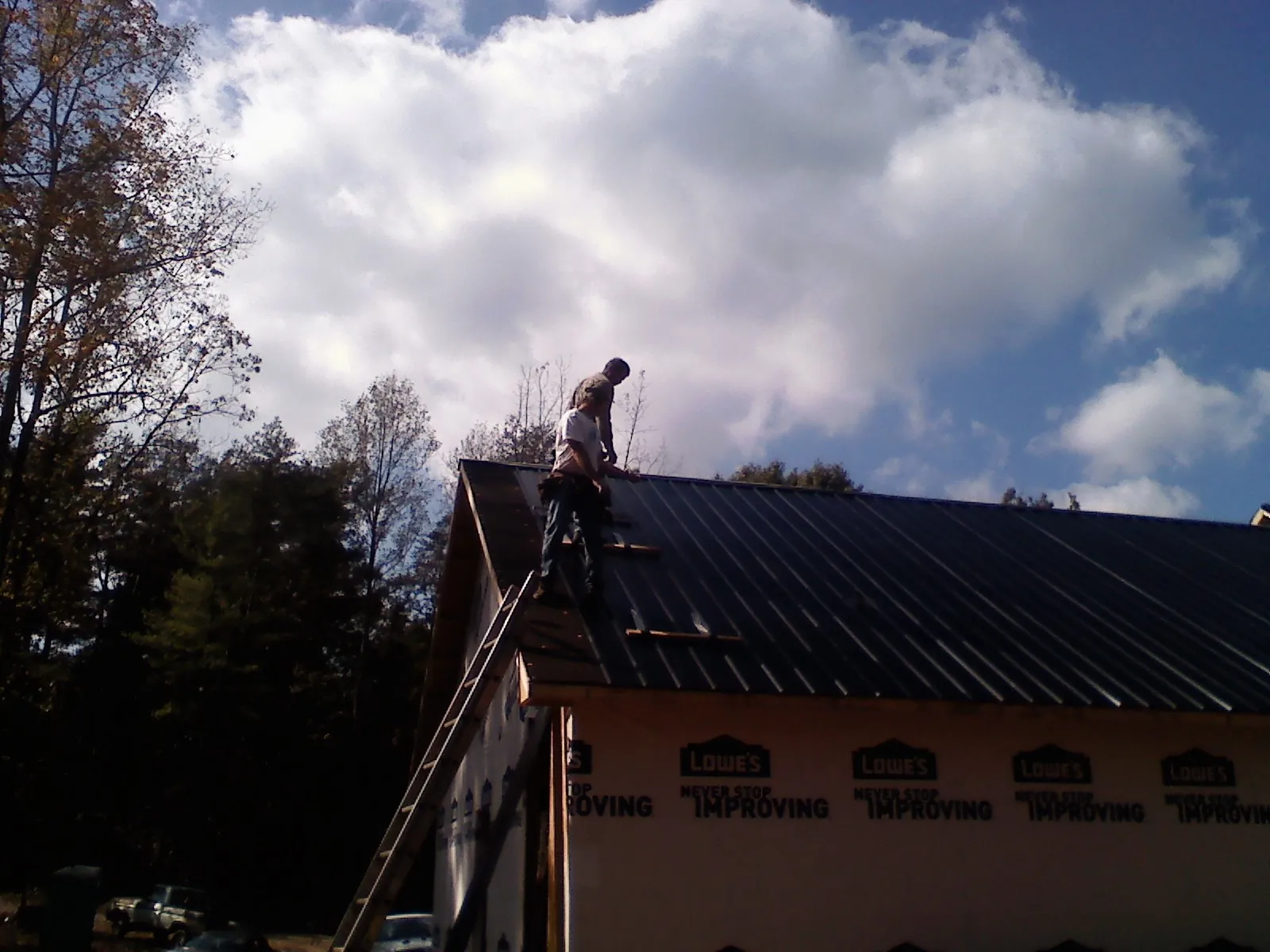 Roofer fastening dark metal panels high against a cloudy sky, from a Roof Inspection job in York Haven