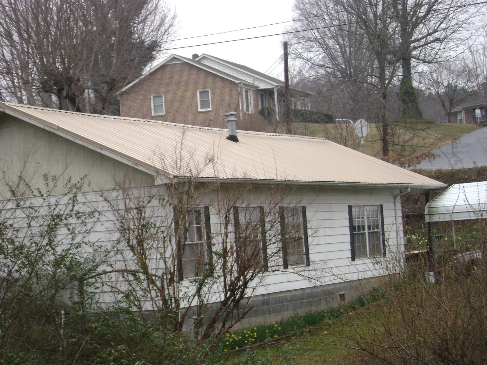 Tan metal roof on a white sided house set into a hillside — Commercial Roofing by Roofing Brothers in York Haven